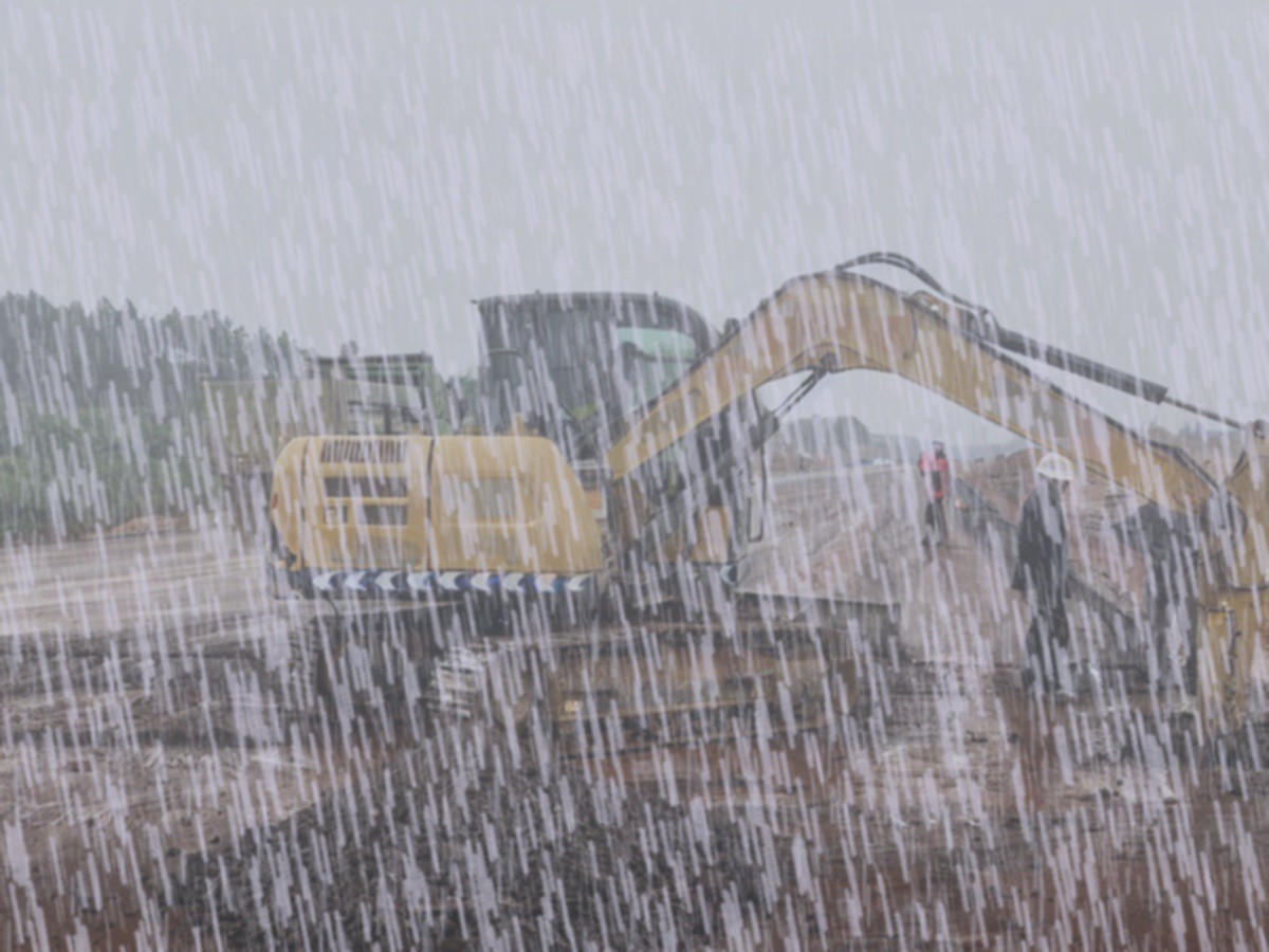 Excavator and workers under heavy rain